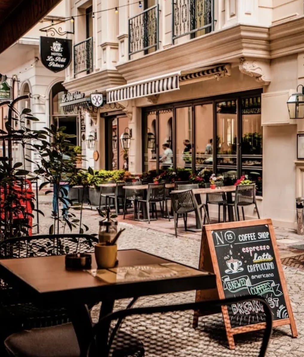 Outdoor coffee shop seating with chalkboard menu — sidewalk café tables, warm string lights, classic European charm